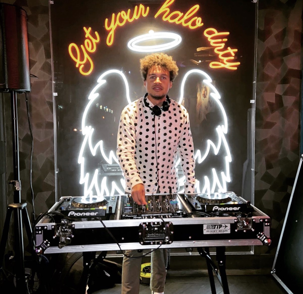 Ollie Pittam DJing at Dirty Martini under a neon angel wings sign